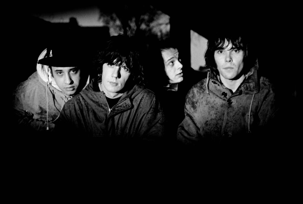 Die vier Bandmitglieder von The Stone Roses sind bei Nacht zu sehen, nur die Gesichter hell erleuchtet.